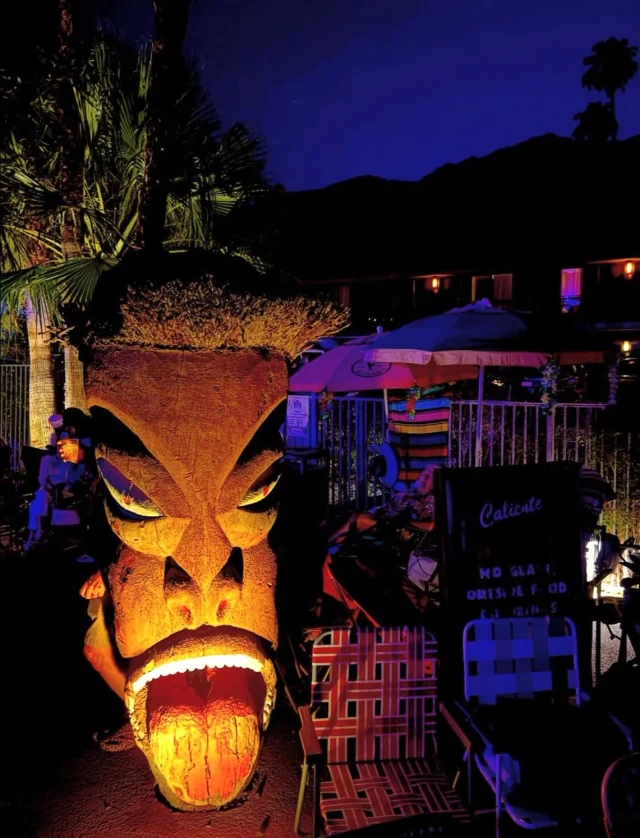 A large tiki statue is lit up at night in front of a pool area.