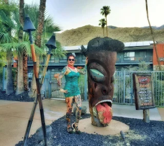 A woman poses next to a large tiki statue in front of a building.